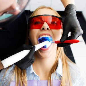 patient-red-glasses-sits-chair-dentist-office-while-doctor-whiten-her-teeth